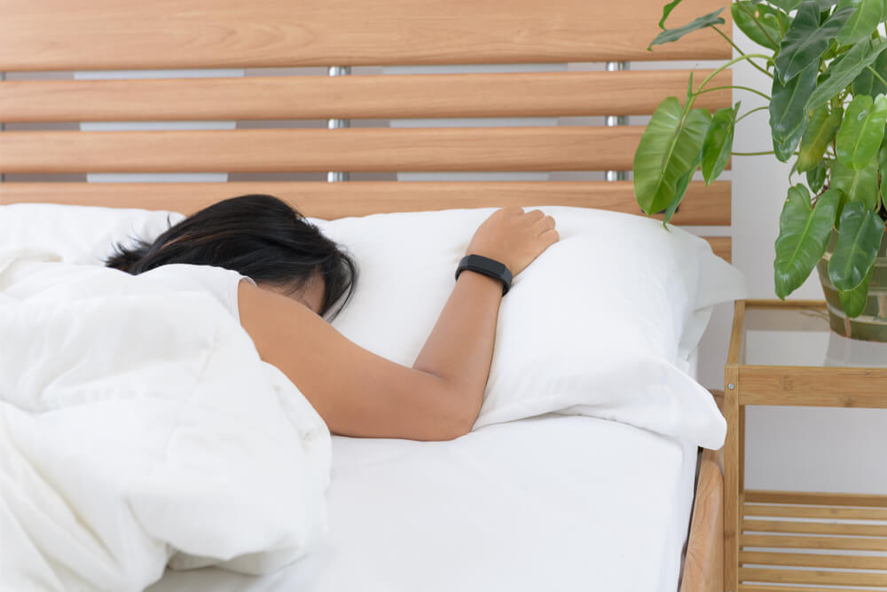 Imagem de uma mulher deitada na cama. Ela está dormindo e utilizando um relógio de monitoramento do sono.