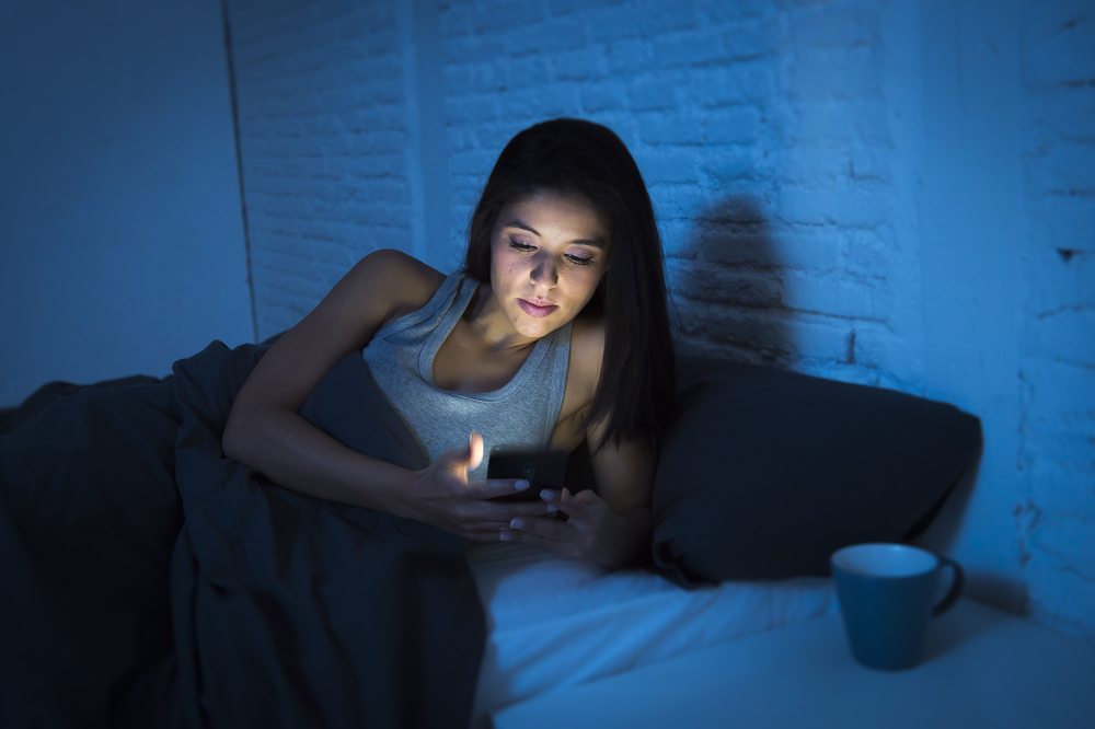 uma mulher sentada na cama olhando para o celular