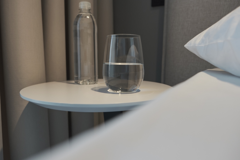 Imagem de um copo d'água e uma garrafa ao lado da cama.