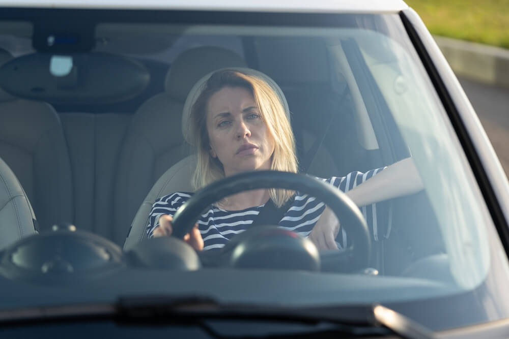 Imagem de uma mulher dirigindo um carro. Ela aparenta estar com sono.