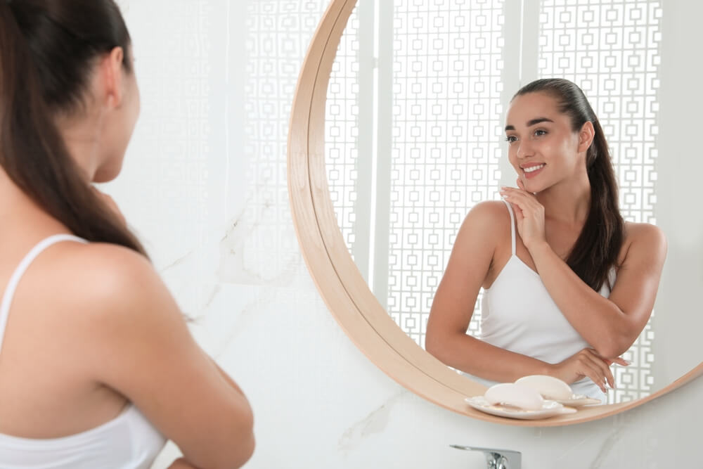 Imagem de uma mulher, em frente a um espelho, acariciando a própria pele.