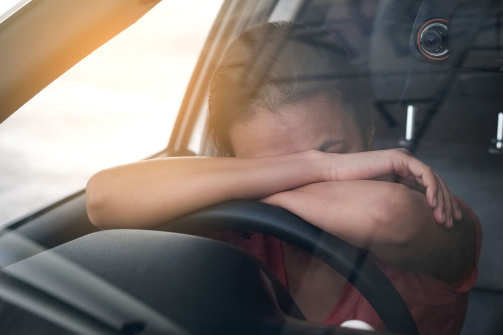 Imagem de uma mulher com sono, deitada sob o volante do carro.