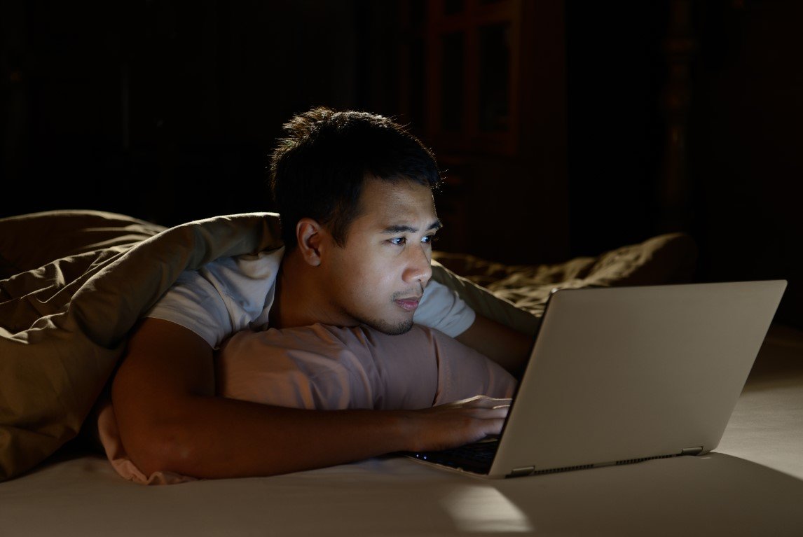 um homem deitado na cama usando um laptop