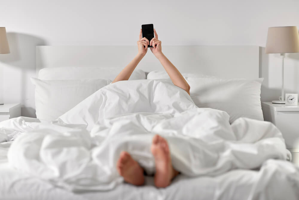 Homem deitado na cama enquanto mexe no celular vendo aplicativos para dormir.