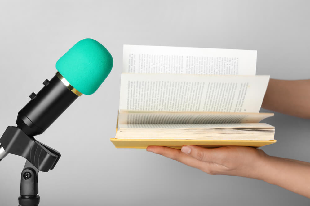 Imagem de mão folheando um livro perto de um microfone.