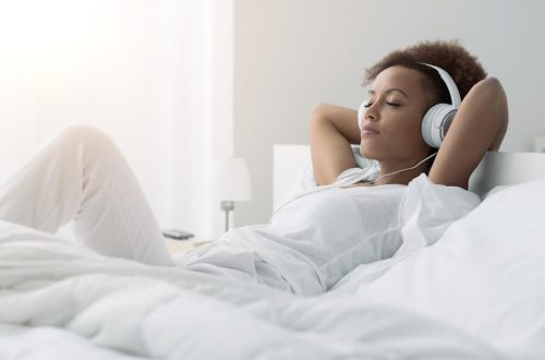Mulher negra deitada em uma cama, com fones de ouvido, relaxando.