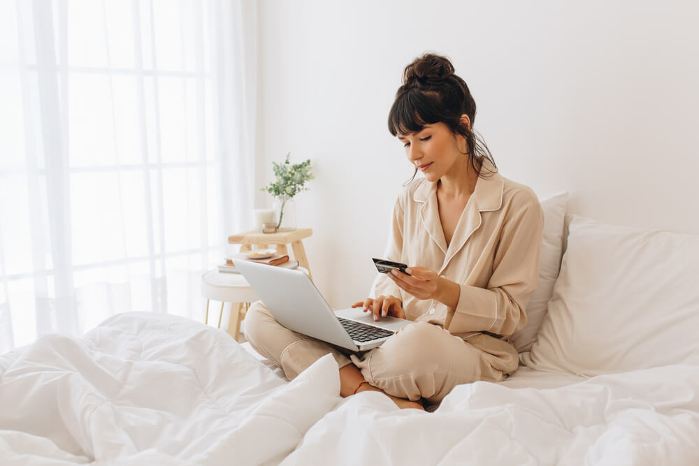 uma mulher sentada em uma cama usando um laptop