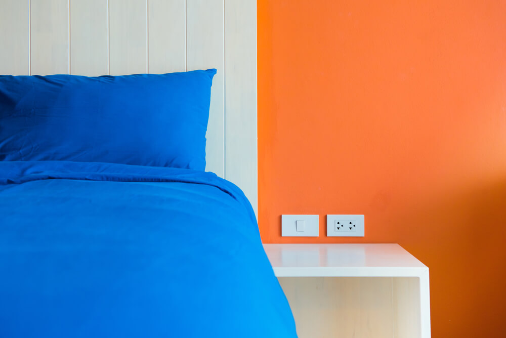 uma cama com edredom azul ao lado de uma parede laranja