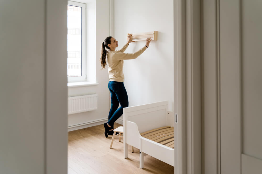 Mulher reformando o quarto gastando pouco. Ela está pregando algo na parede.