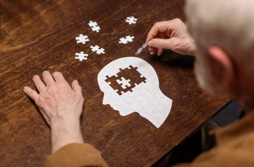 Imagem de um senhor sentado em uma mesa. Ele está montando um quebra-cabeça que tem formato de tronco humano. No cérebro, está faltando uma peça.