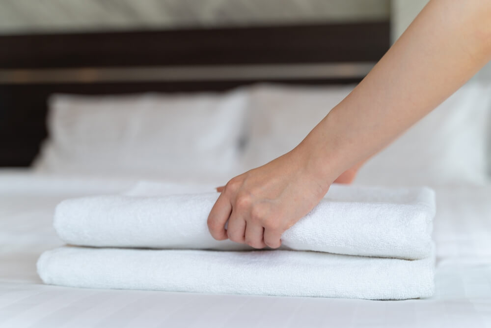 Imagem de um lençol sendo dobrado, em cima de uma cama.