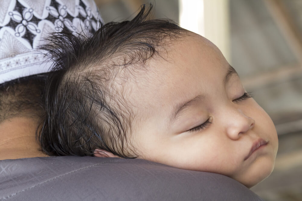 Bebê dormindo no colo de uma mulher, com o cabelinho molhado de suor.