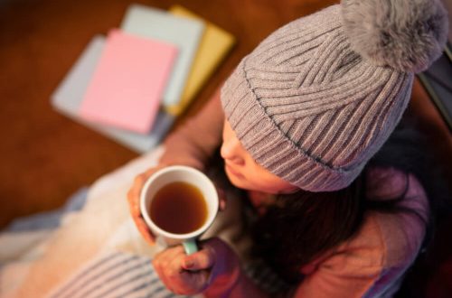 Imagem de uma mulher com uma touca na cabeça, segurando uma caneca de chá para tomar a noite.