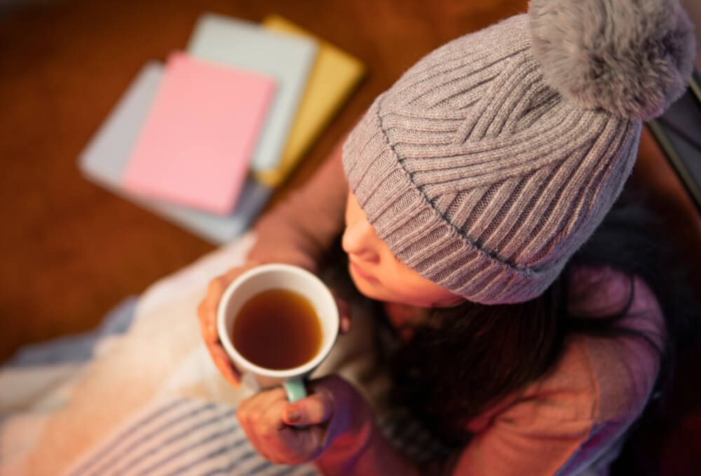 Imagem de uma mulher com uma touca na cabeça, segurando uma caneca de chá para tomar a noite.