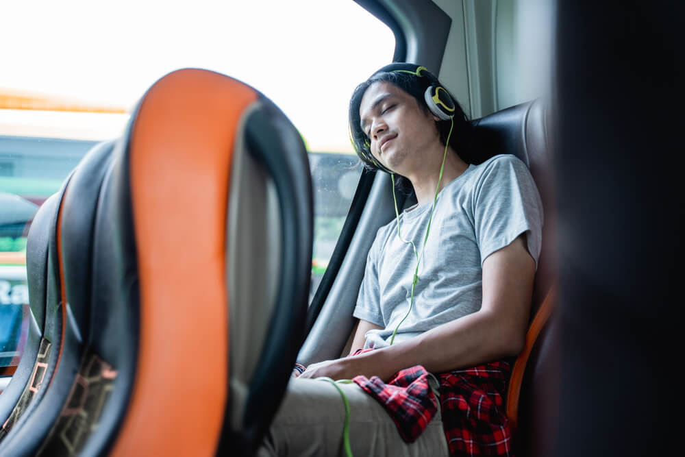 Pessoa deitada no ônibus, com fone de ouvido nas orelhas.