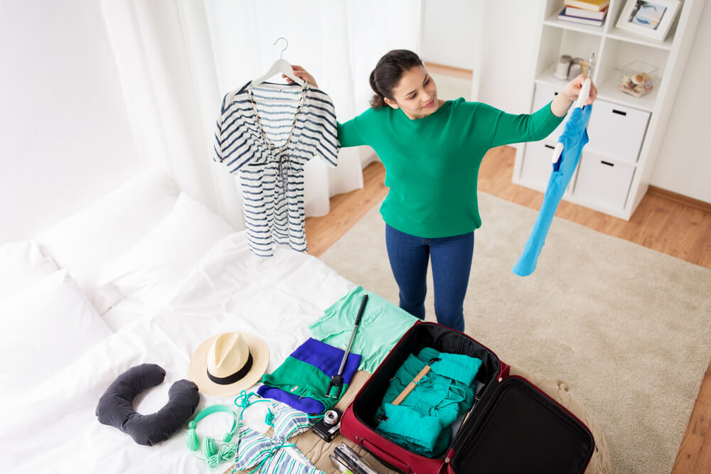 Imagem de uma mulher arrumando as malas e decidindo qual roupa utilizar para viajar.