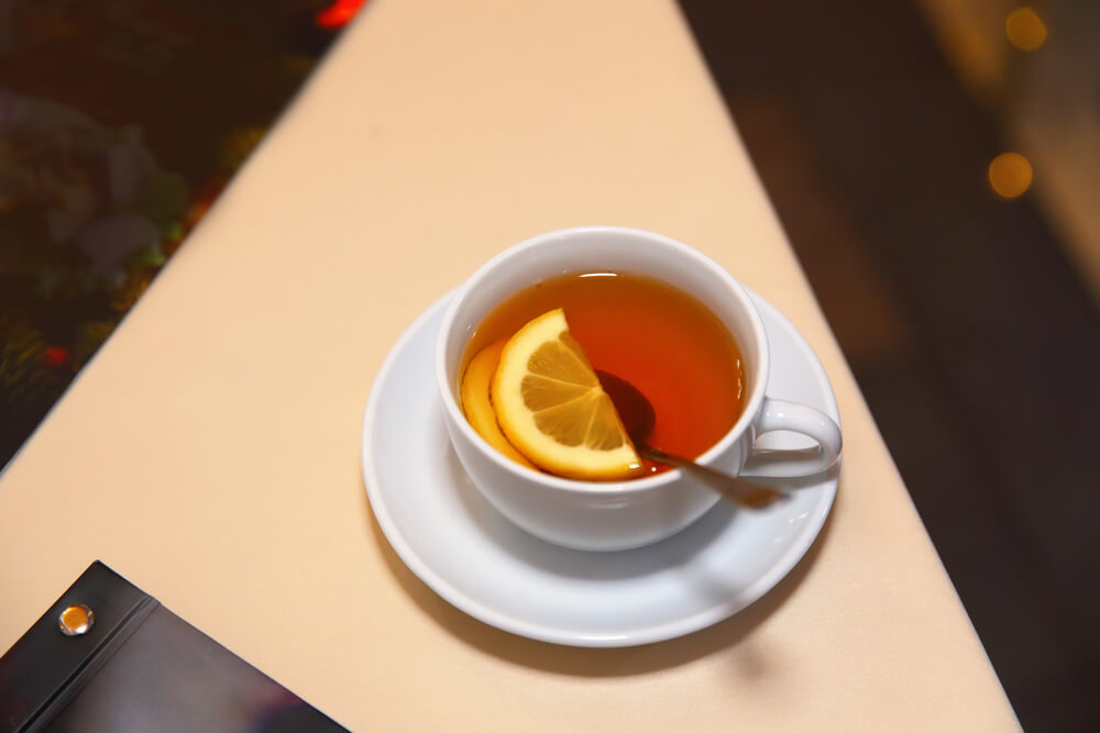 Imagem de uma xícara de chá. Dentro dela há uma colher e metade de uma fatia de laranja.