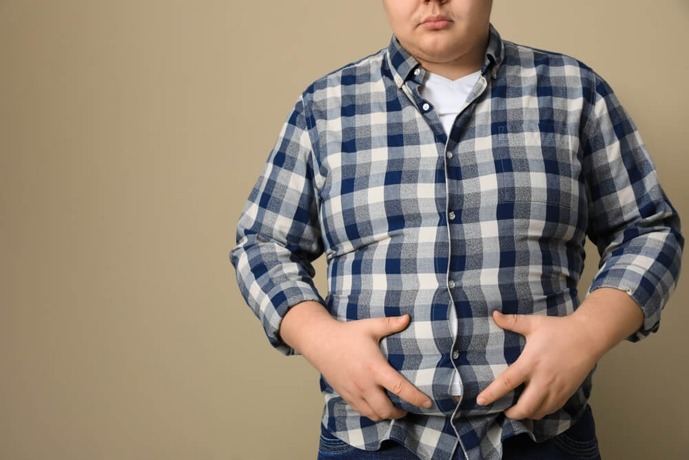 Imagem de um homem, com obesidade. Ele está apertando a própria barriga.