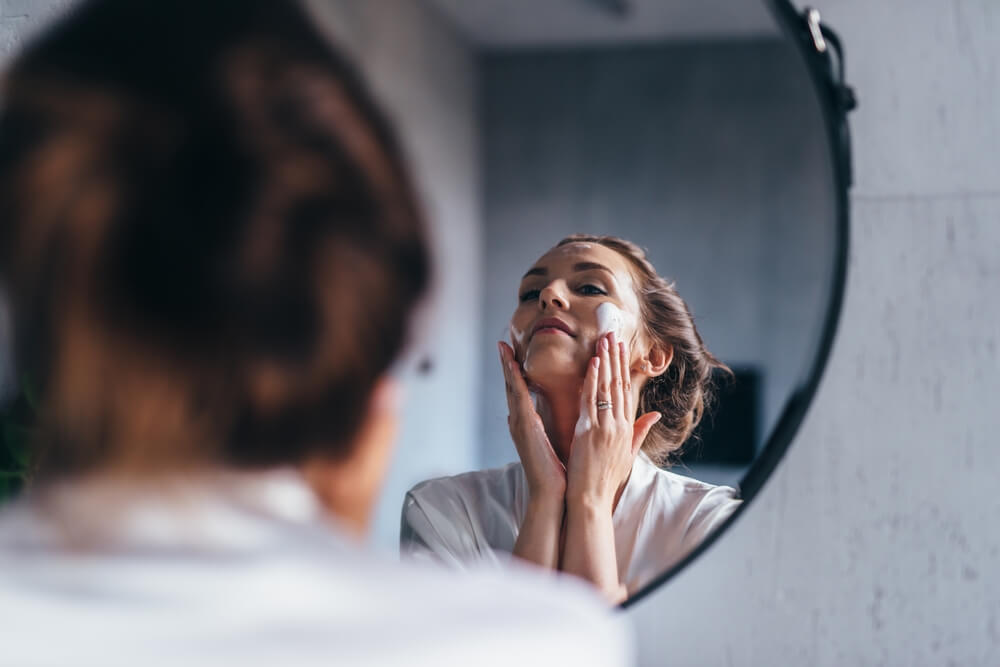 Imagem de uma mulher, em frente ao espelho, fazendo skincare.