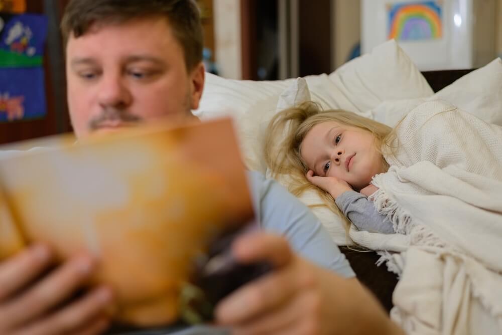 Imagem de um pai lendo para filha antes de dormir.