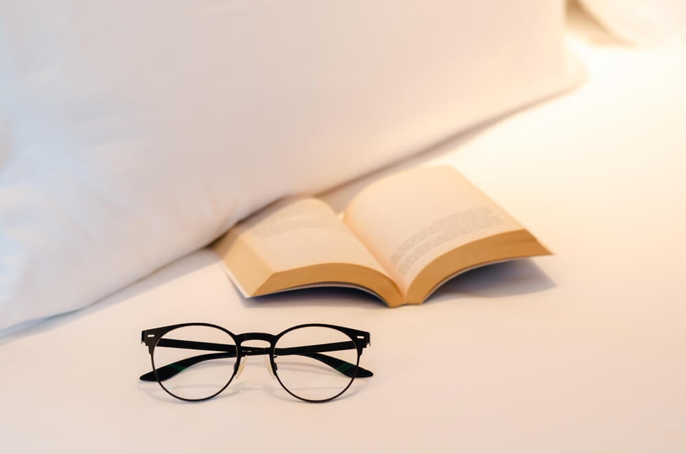 um par de óculos em cima de uma cama ao lado de um livro aberto