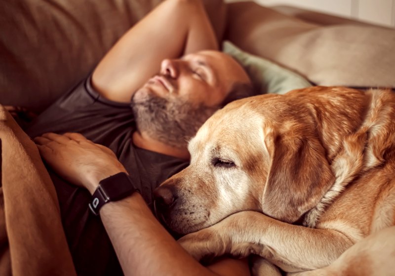 um homem deitado em um sofá ao lado de um cachorro