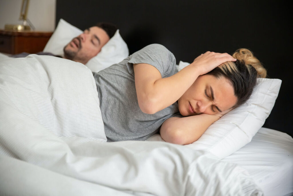 casal dormindo na cama e a mulher com o travesseiro nos ouvidos