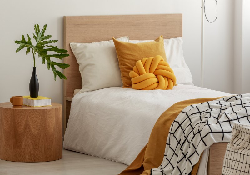 cama com cabeceira de madeira, lençol branco e almofada amarela
