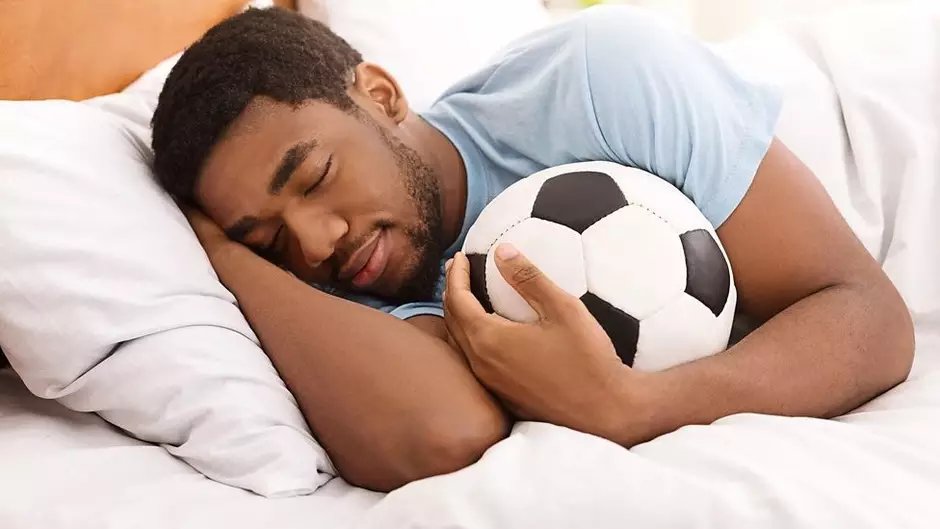 um homem dormindo na cama com uma bola de futebol