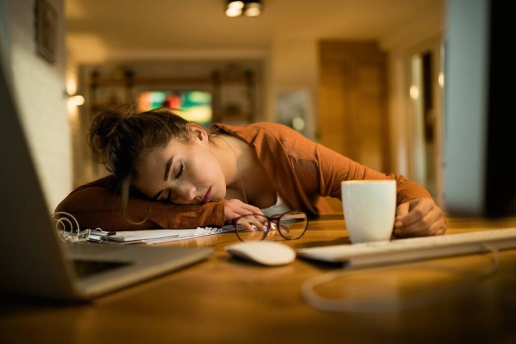 jovem mulher cansada cochilando em sua mesa enquanto trabalhava tarde da noite em casa