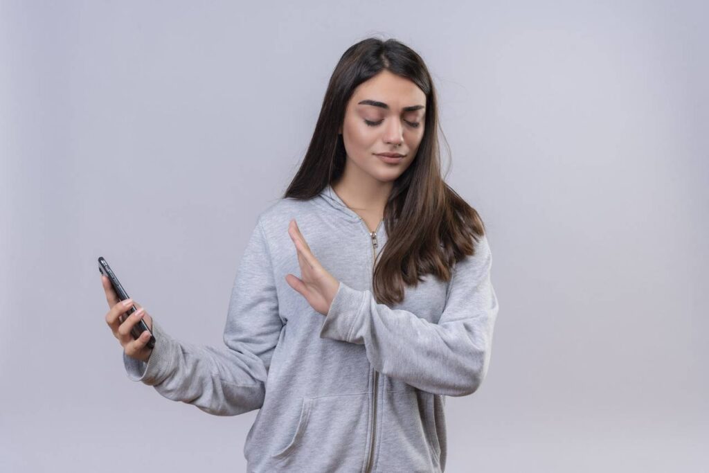 menina linda em um casaco com capuz cinza segurando o telefone sem olhar para o telefone em pe sobre um fundo branco